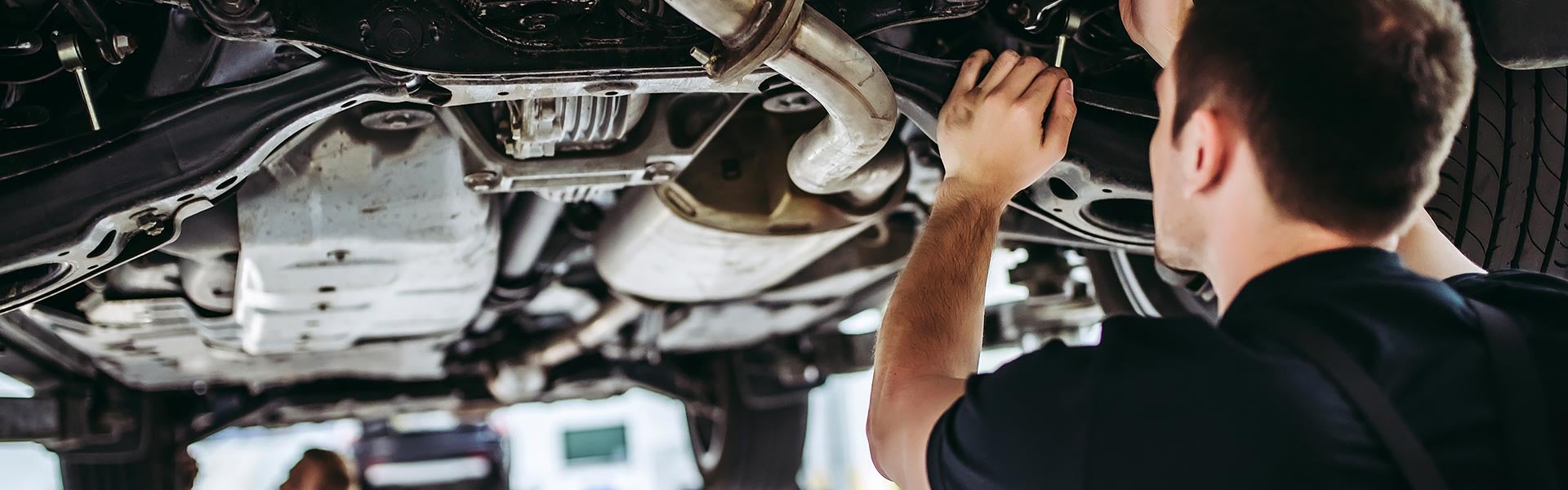 Auto mechanic inspecting the underside of a vehicle during routine maintenance.