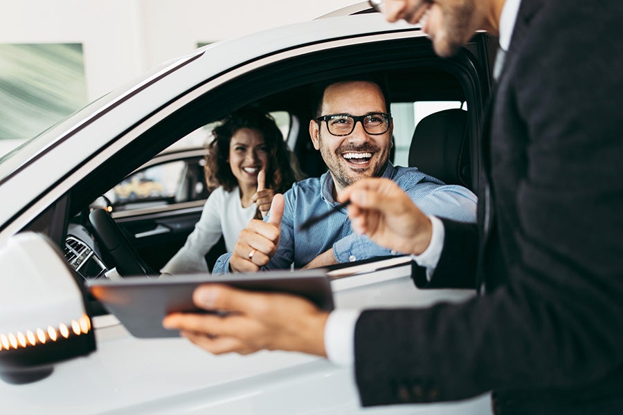 Two people sitting in a car looking at a salesman's tablet